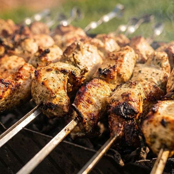 Marinated chicken skewers grilling over hot coals with smoke rising, ready to be served.